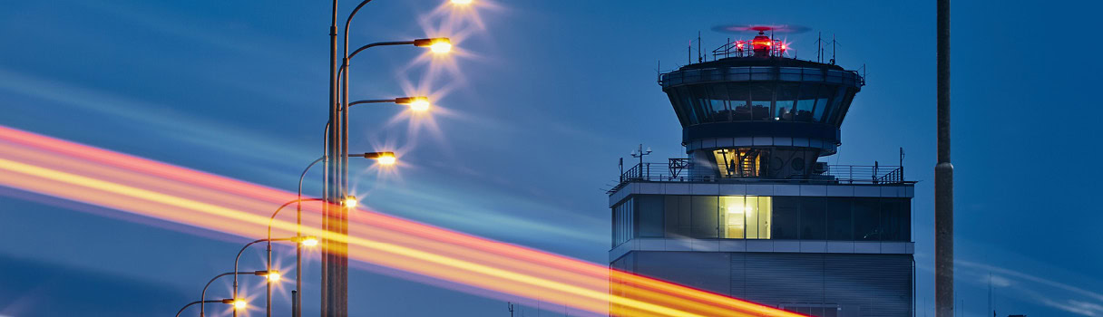 Time Synchronization_ATC Airport control tower at night with glowing strips of light from passing vehicles, symbolizing time synchronization.