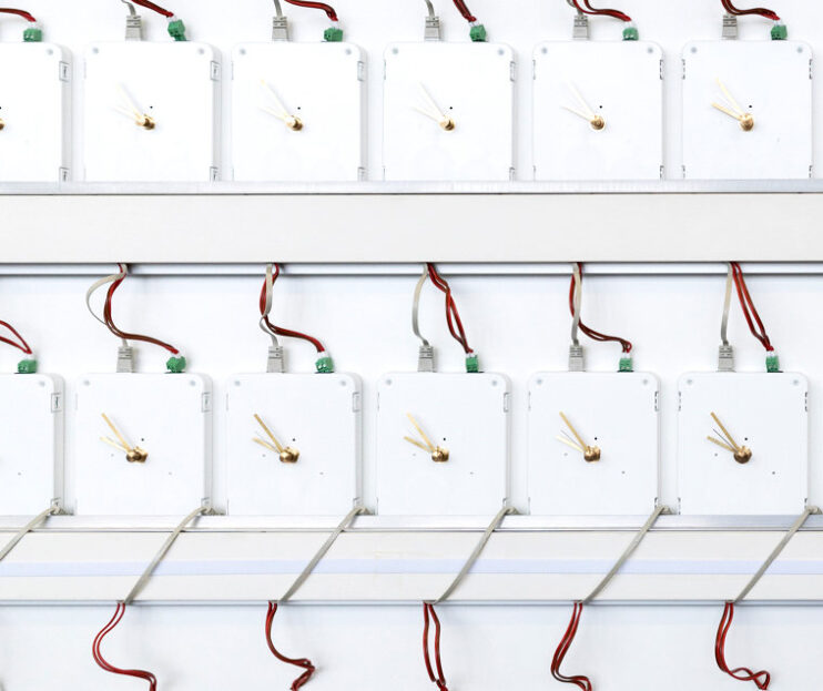 A precision array of MOBATIME synchronized analog clocks wired for unified timekeeping, against a white backdrop